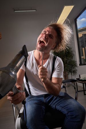 Excited man singing in hair dryer and hairbrush
