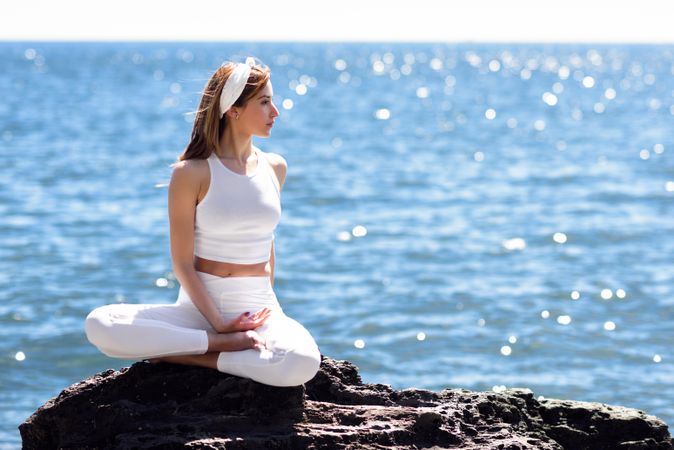 Young woman stretching her back in lotus pose on rocky beach