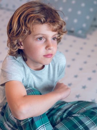 Adorable little boy sitting on bed and dreaming