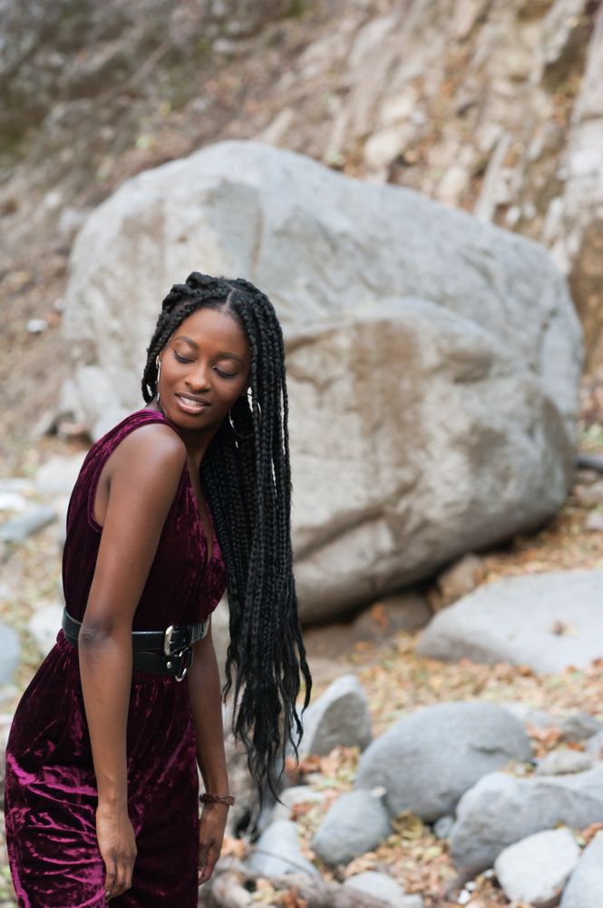 Fashionable woman with long braids in front of a boulder