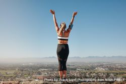 Woman in fitness wear standing on the edge of a hill looking at the city below 4jKAJb