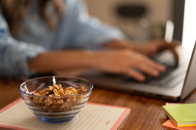 Bowl of walnuts on a desk with a person typing on a laptop