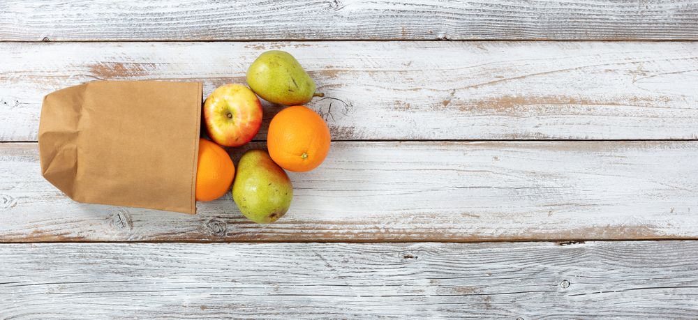 Fresh organic fruit pouring out of recyclable paper bag