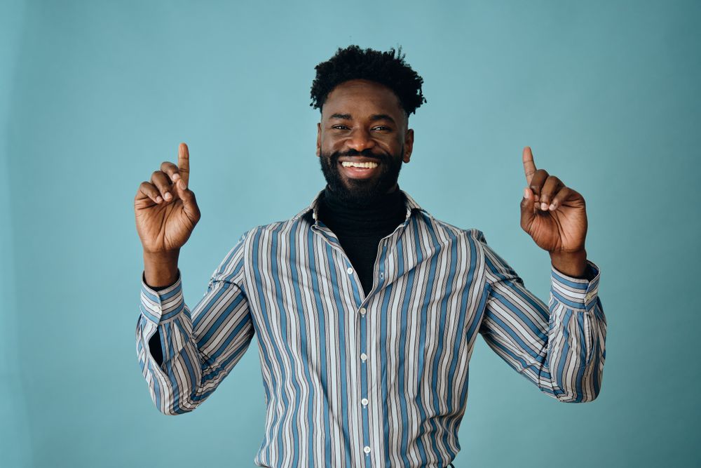 Smiling Black man in blue striped shirt pointing up with both hands