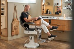 Concentrated barber sitting on chair with magazine in salon