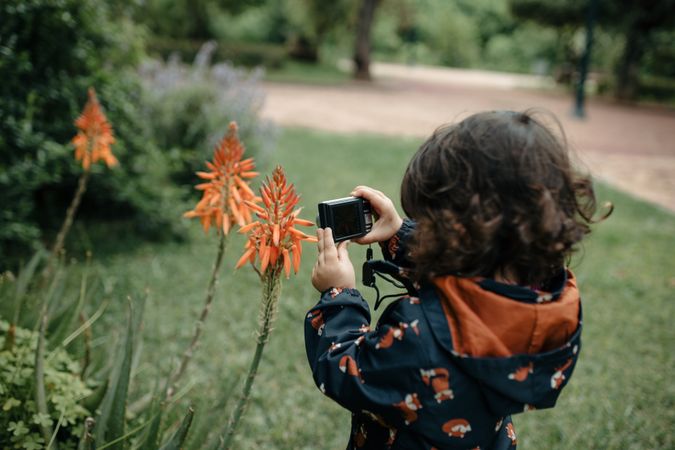 Little girl holding camera up close to aloe flowers to take a photo