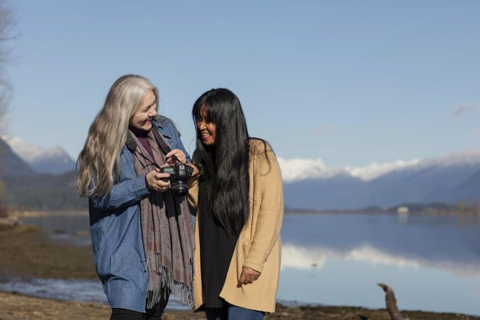 Happy women reviewing photos on a camera next to a lake
