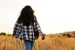 Young woman taking photos with analog camera in the field at sunset