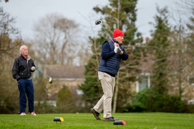 Mature male swinging golf club with friend looking on