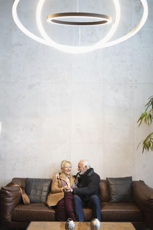 Mature couple sitting on leather sofa together, vertical