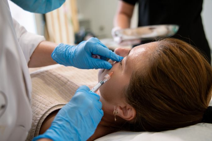 Anonymous beautician administering injection to cheek of female client