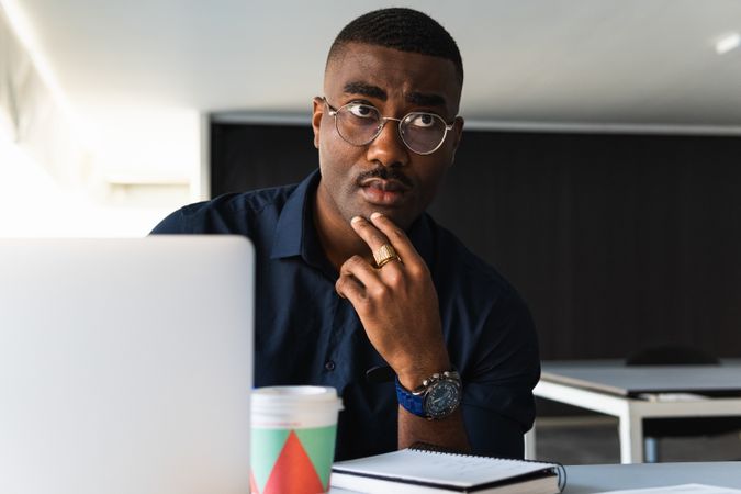 Black man writing in notepad near laptop in office