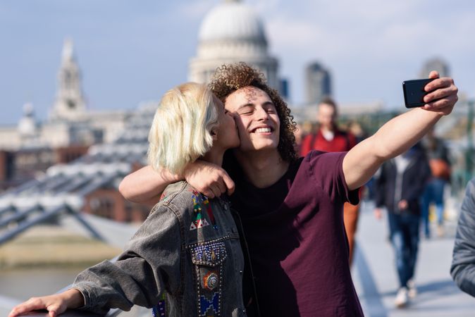 Blonde female and curly haired boyfriend taking selfie on bridge in London
