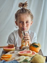 Smiling little boy sitting at table and drinking juice