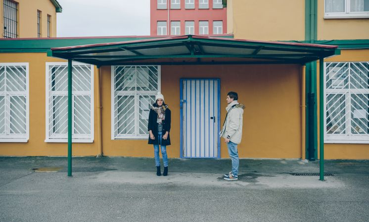 Couple wearing winter clothes standing under a metallic roof outdoors in a cold and rainy day