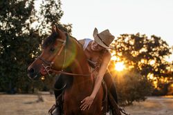 Young woman in hat riding a horse in the countryside at sunset