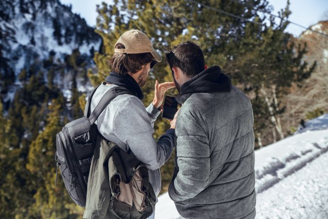 Men with smartphone and camera on hill between trees in winter