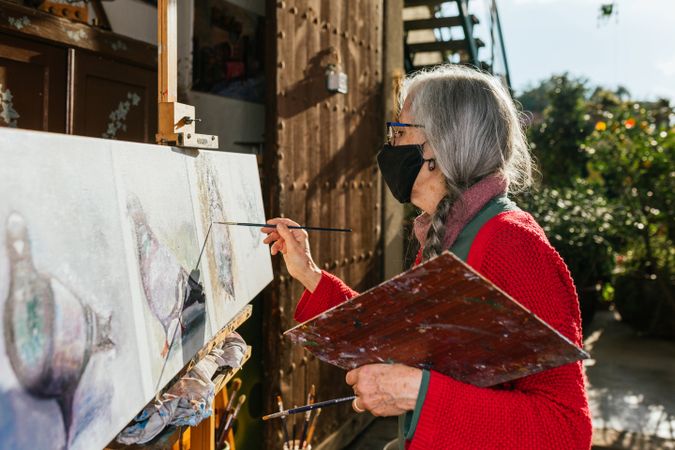 Older woman painting on canvas in garden