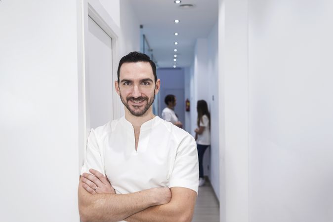 Portrait of a bearded male dentist standing with arms crossed in hallway
