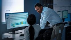 Colleagues Analyze Financial Data on Large Monitor in Dimly Lit Office.