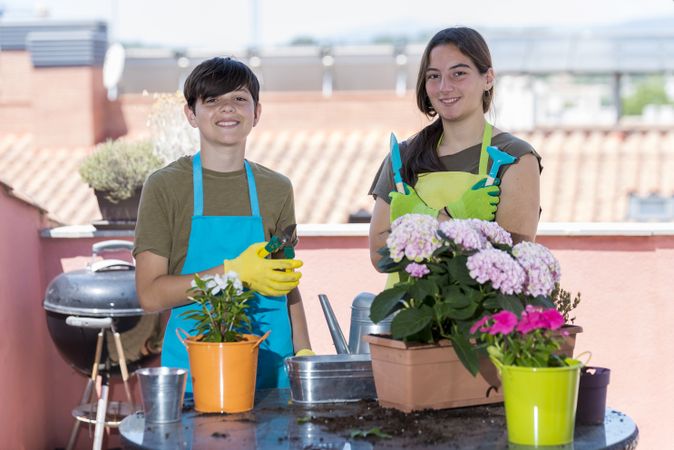 Two happy teenagers wearing gardener apron posing with their plants on home terrace