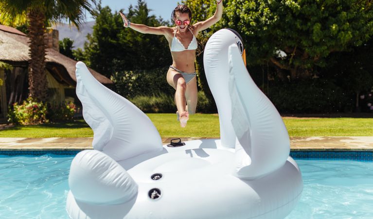 Cheerful woman jumping on inflatable toy in swimming pool