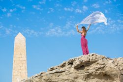 Woman in dress with scarf in upped hands near stone monument