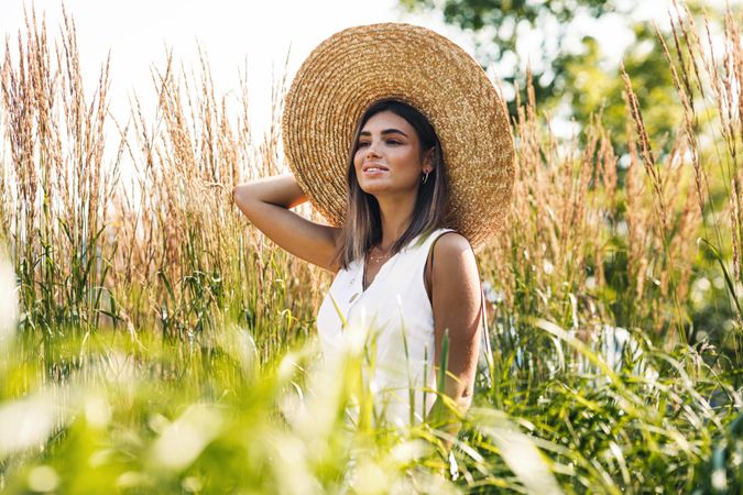 Smiling woman in straw hat standing outside in long grass