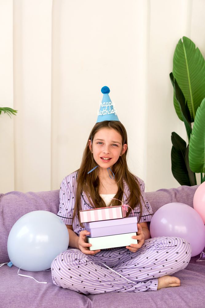 Young girl celebrating birthday at home with presents and balloons.