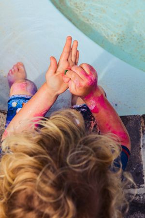 Top view of blond boy washing pink paint off his hands with a sponge