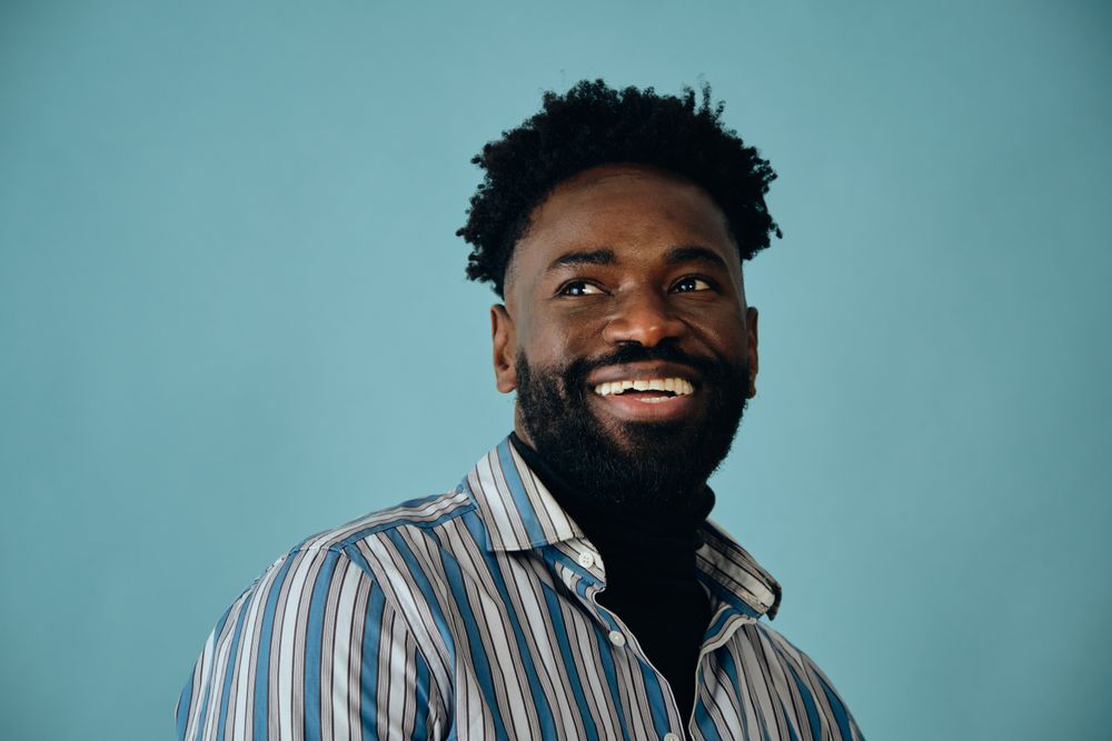 Closeup portrait of a smiling Black man in blue studio shoot looking away from the camera