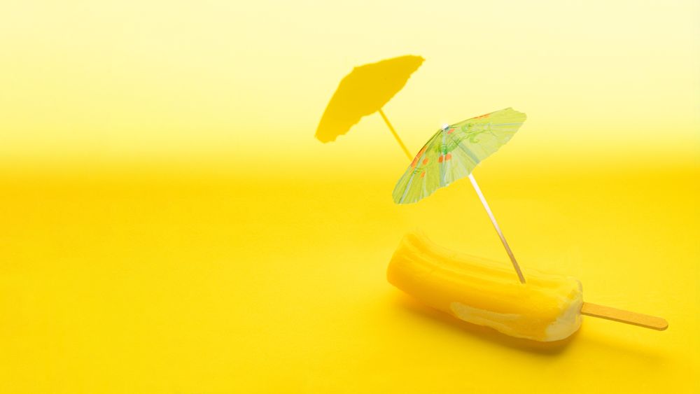 Ice pops with two cocktails parasols melting on yellow background