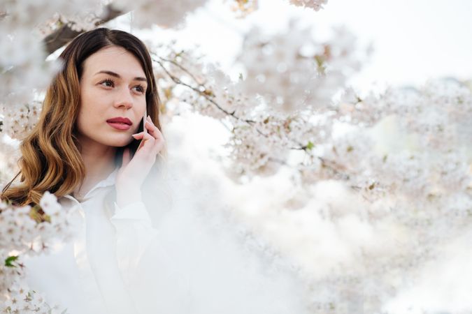 Woman answering phone call near blooming trees