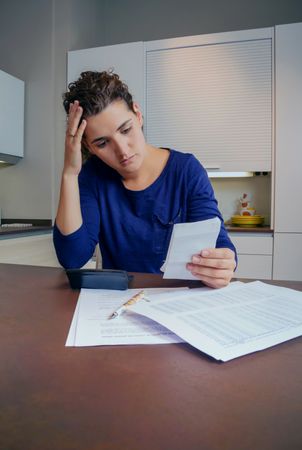 Stressed woman reviewing bills at kitchen counter