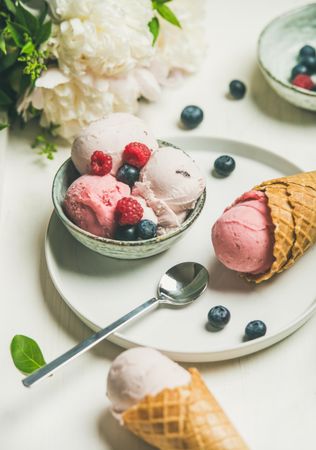 Scoops of ice cream in bowl and in waffle cones with berries