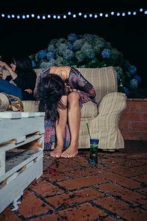 Young drunk woman sitting on the sofa on a party with her head in her lap