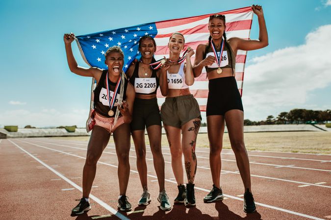 Happy multiracial athletes celebrating victory while standing together on racetrack