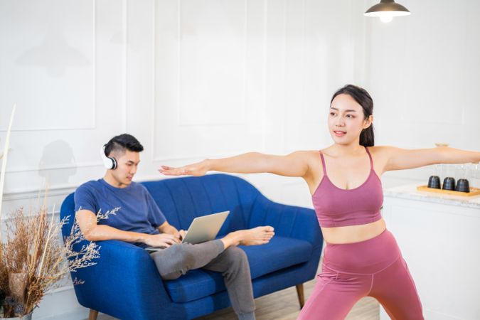Woman in warrior pose with her partner on sofa in the background