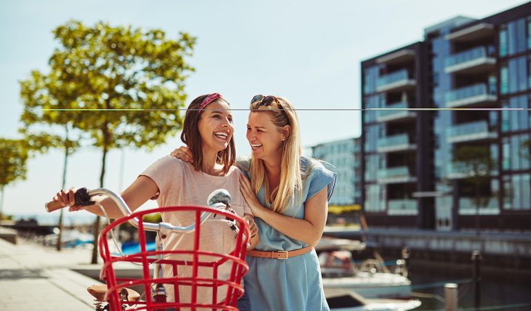 Two women laughing while walking with a bicycle along the river walk