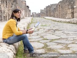Side view of a woman in yellow clothes sitting while checking tourist map of ancient ruins 432lNO