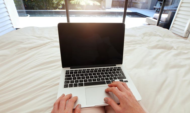 Closeup image of woman on a bed working on laptop
