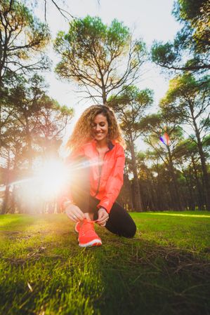 Woman tying shoelaces on meadow in sunlight