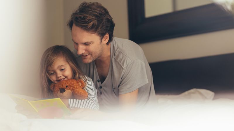 Dad and little girl reading a book with her teddy bear