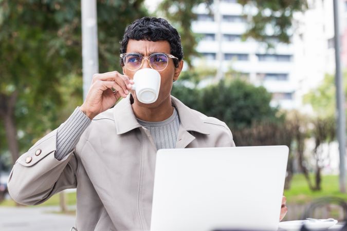 Focused hispanic man using laptop and drinking coffee