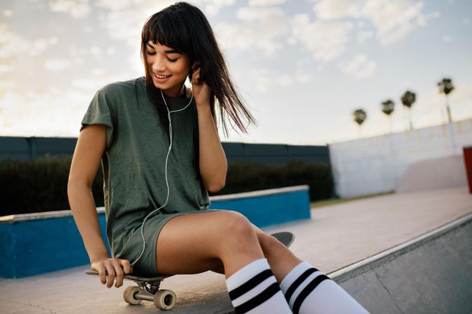 Female skateboarded relaxing at skate park listening music