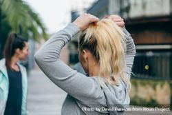 Back of blonde woman runner tying her hair in a ponytail before training bE9pRo