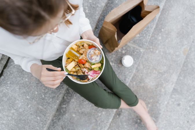 Top view of woman eating a salad sitting on gray steps outdoor