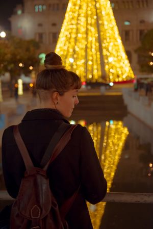 Woman in trendy outfit looking at beautiful shining Christmas tree