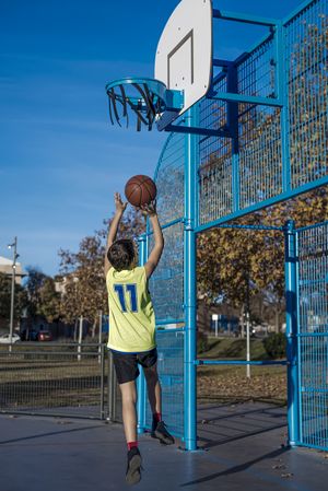 Teenager throwing a basketball into blue hoop from behind