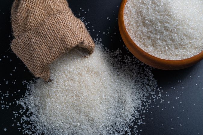 sugar spilling from a burlap sack beside a full bowl
